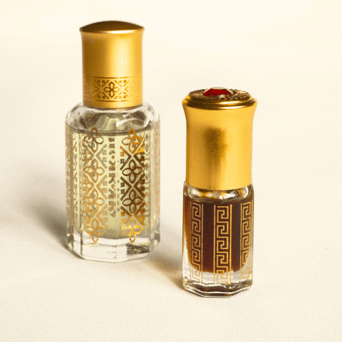 Two ornate glass bottles of Arabian attar perfume with gold caps on a neutral background.